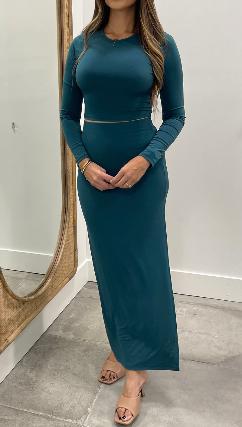 Woman wearing a teal dress standing in front of a mirror.