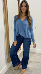 Woman wearing a blue long-sleeve top and jeans standing in front of a mirror.