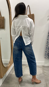 Person wearing a white shirt and blue jeans standing in front of a mirror.