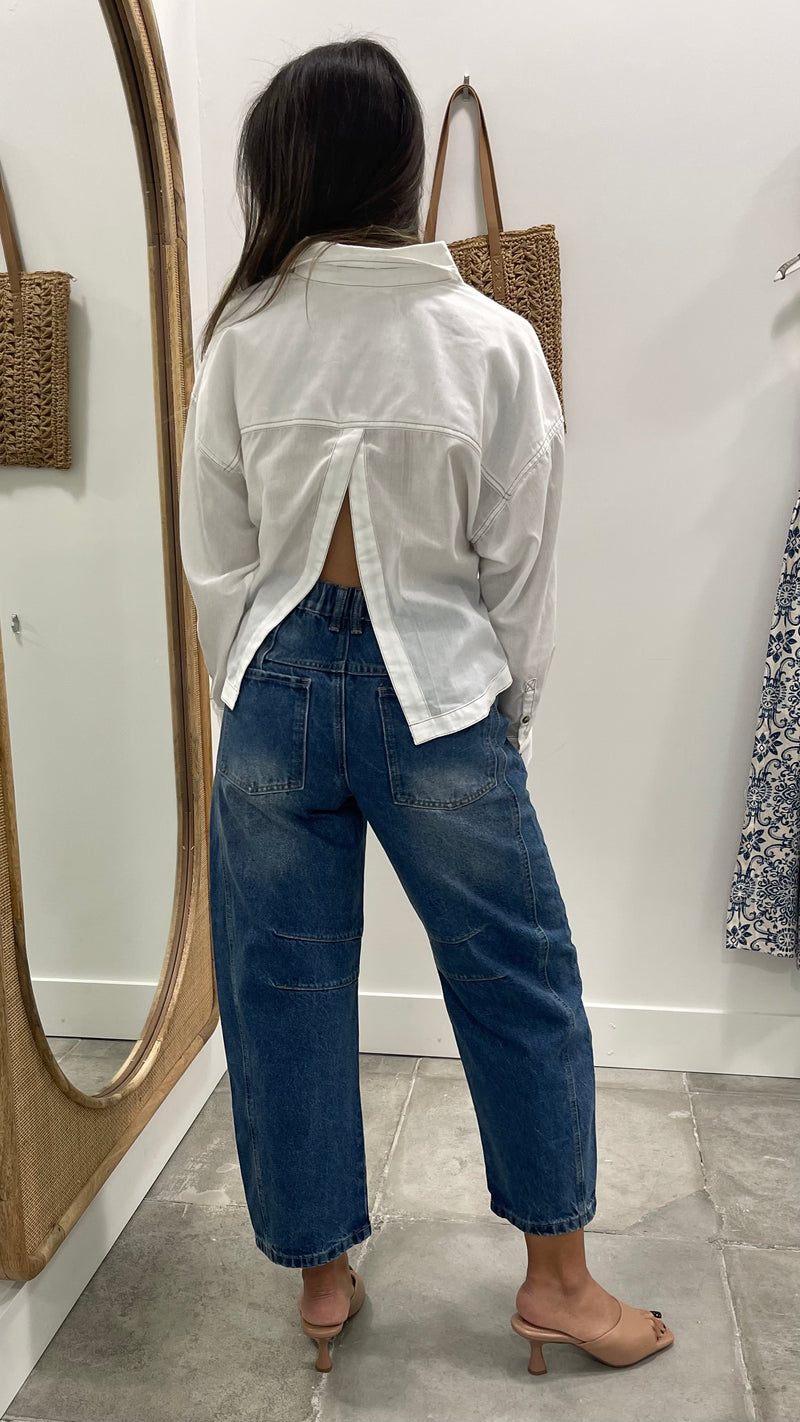 Person wearing a white shirt and blue jeans standing in front of a mirror.
