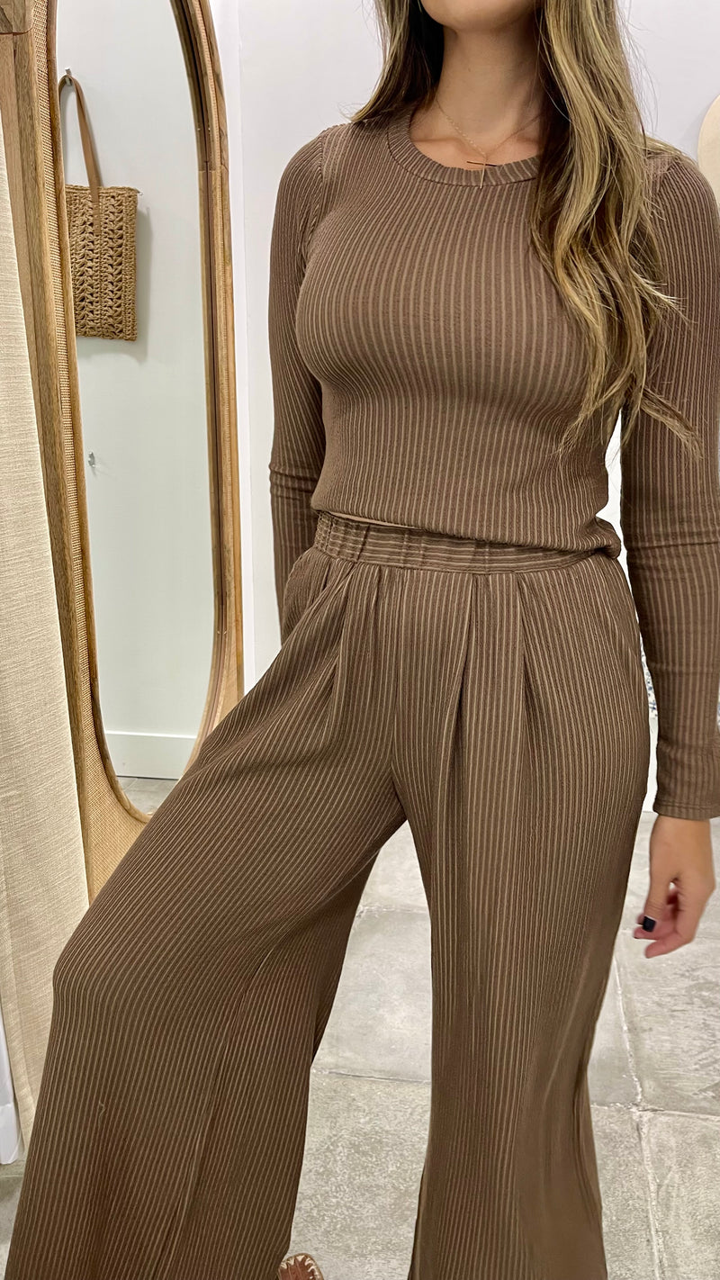 Woman wearing a brown ribbed top and wide-leg pants in a neutral setting.