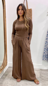 Woman wearing a brown ribbed top and wide-leg pants standing in front of a mirror.