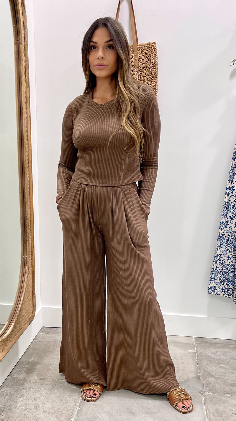 Woman wearing a brown ribbed top and wide-leg pants standing in front of a mirror.