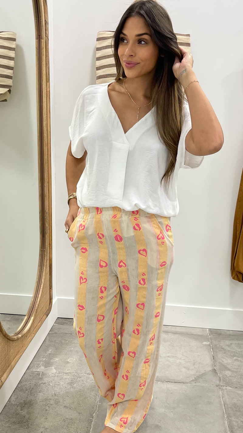 Woman wearing a white blouse and patterned pants standing in front of a mirror.