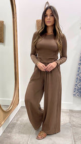 Woman wearing a brown ribbed top and wide-leg pants standing in front of a mirror.