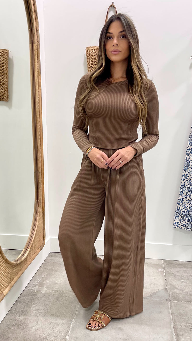 Woman wearing a brown ribbed top and wide-leg pants standing in front of a mirror.