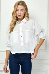 Woman wearing a white shirt with rolled-up sleeves and blue jeans against a white wall.