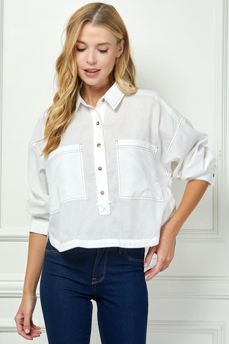 Woman wearing a white shirt with rolled-up sleeves and blue jeans against a white wall.