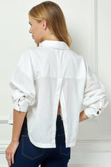 Woman wearing a white denim jacket and blue jeans against a white wall.