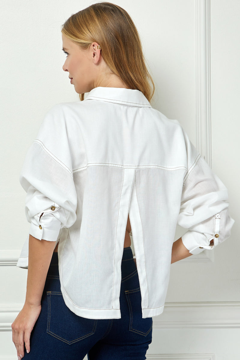 Woman wearing a white denim jacket and blue jeans against a white wall.