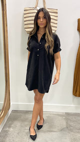 Woman wearing a black dress standing in front of a mirror.