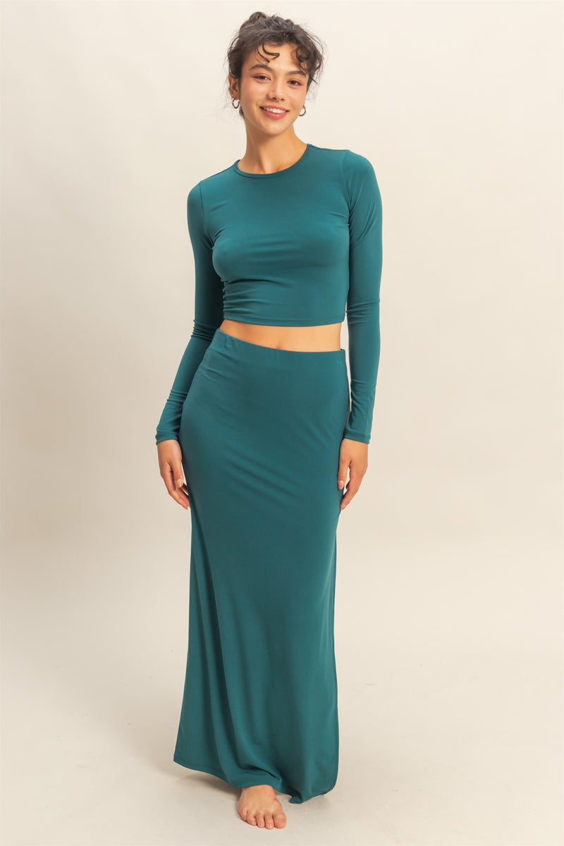 Woman wearing a teal long-sleeve top and matching skirt on a beige background