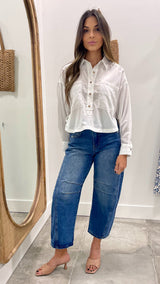Woman wearing a white shirt and blue jeans standing in front of a mirror.
