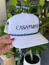 White hat with 'CASA MIAM' text held by a hand against a blurred indoor background
