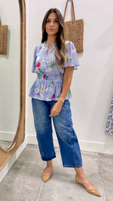 Woman wearing a floral blouse and blue jeans standing in front of a mirror.