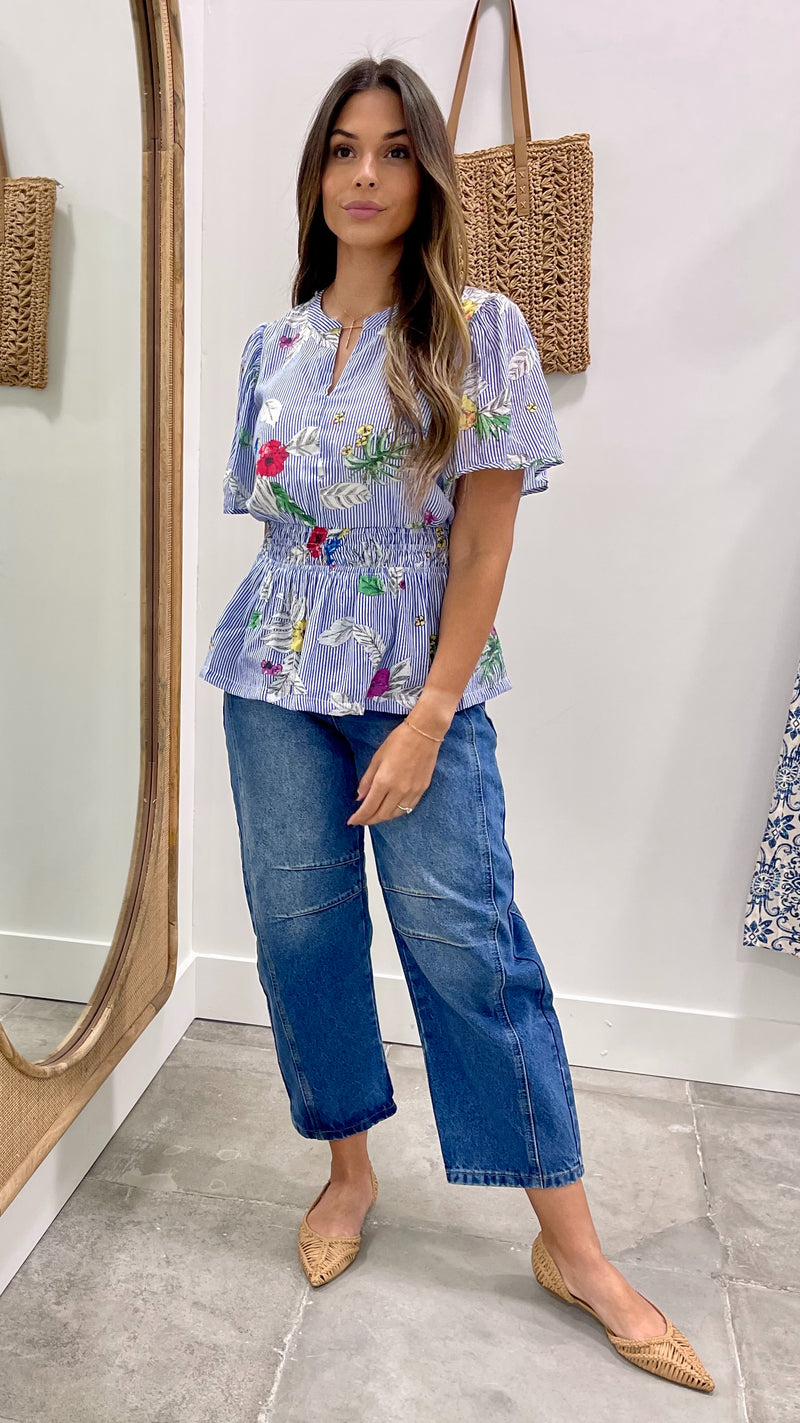 Woman wearing a floral blouse and blue jeans standing in front of a mirror.