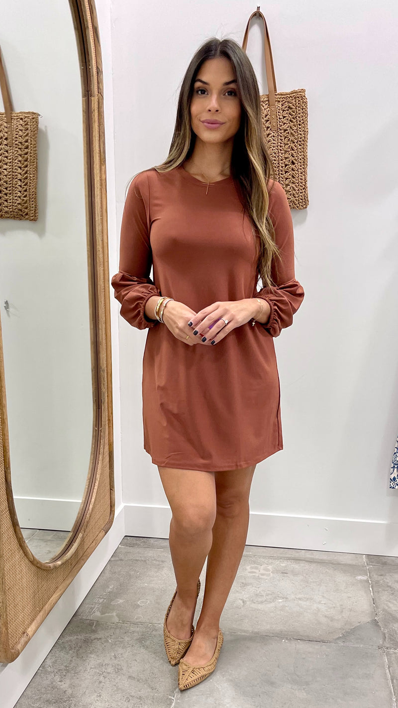 Woman wearing a brown dress standing in front of a mirror.