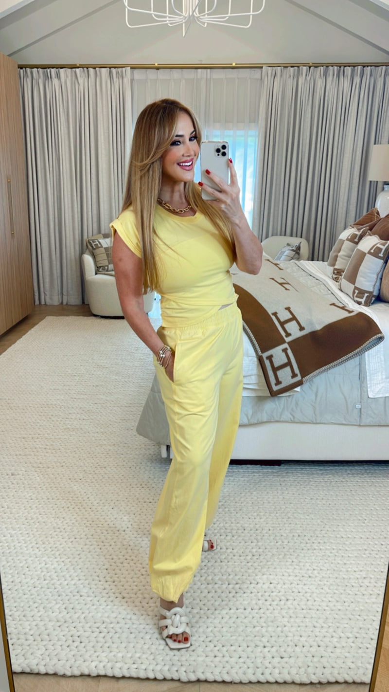 Woman in a yellow outfit taking a mirror selfie in a bedroom.