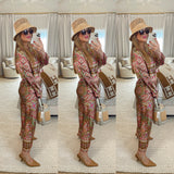 Woman in a patterned outfit with a hat and sunglasses, holding a bag, in a room with a couch and rug.