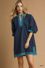 Woman wearing a navy dress with turquoise trim on a beige background