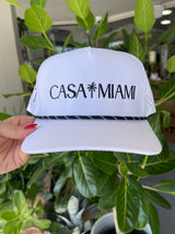 White visor with 'Casa Miami' text held in front of green plants