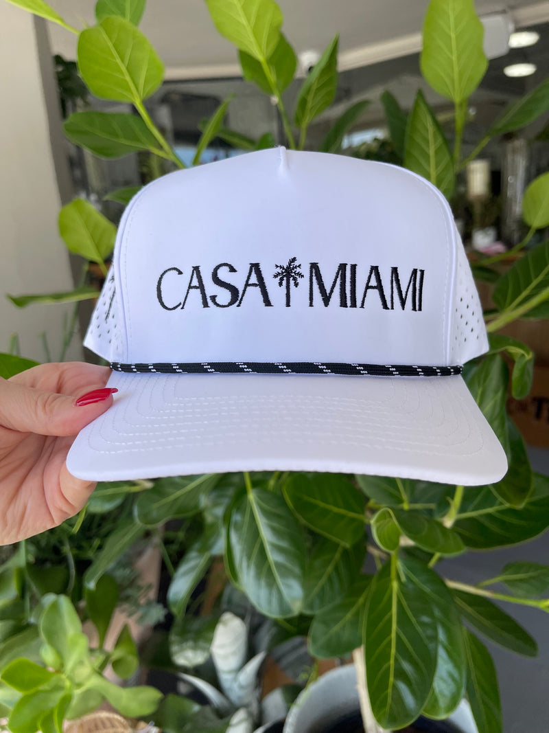 White visor with 'Casa Miami' text held in front of green plants