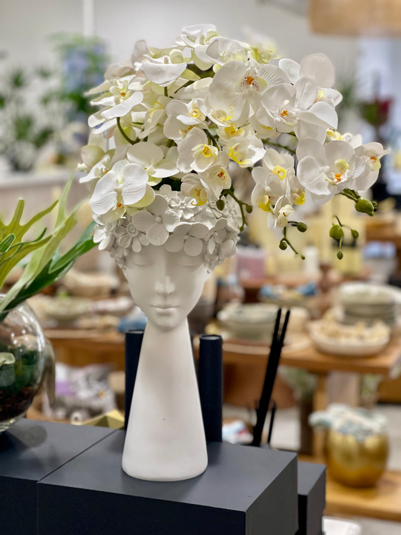 White flowers in a vase shaped like a face on a black surface with a blurred background