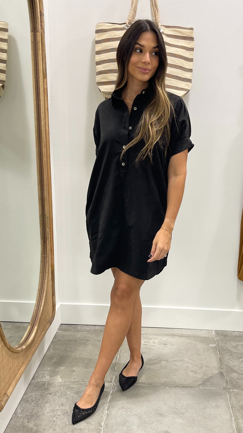 Woman wearing a black dress standing in front of a mirror.