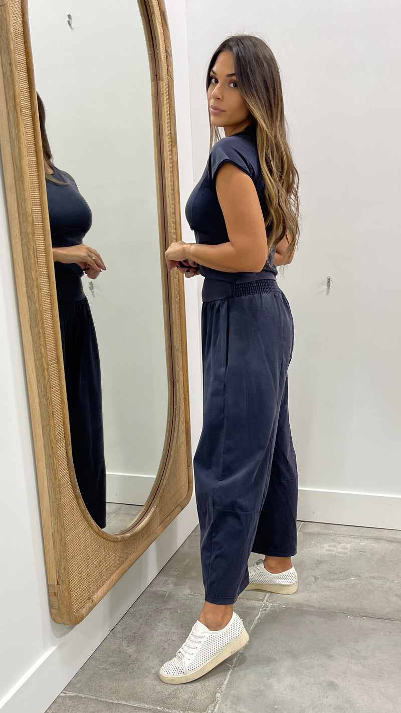 Woman in a navy jumpsuit standing in front of a mirror.