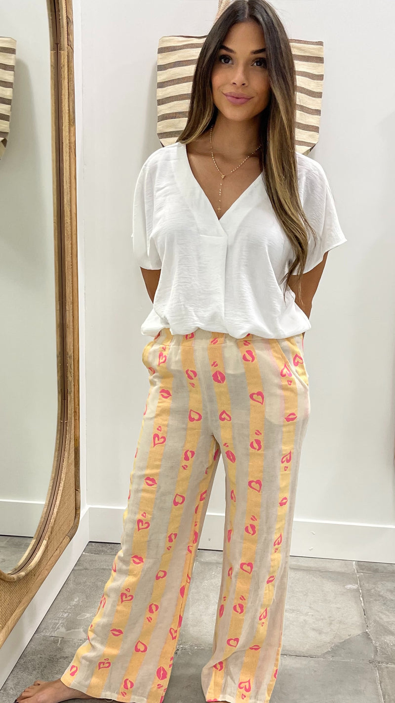 Woman wearing a white blouse and yellow striped pants in a room with a mirror and striped chair.
