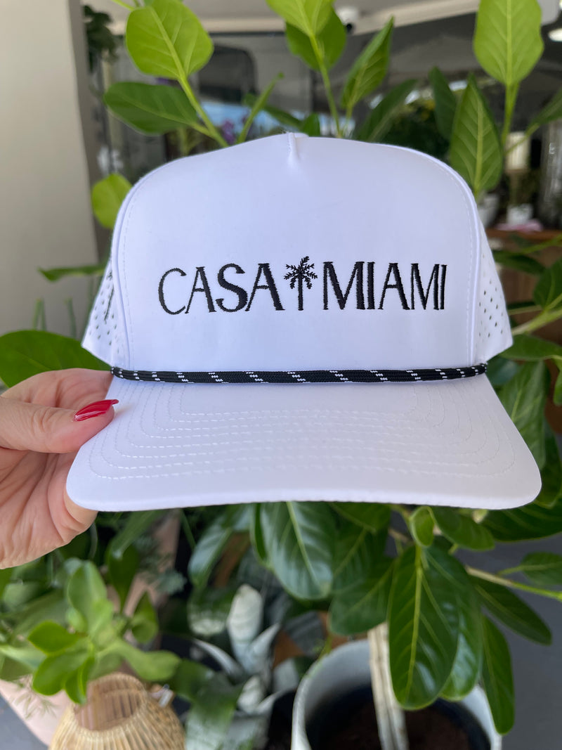 White visor with 'Casa Miami' text held in front of green foliage