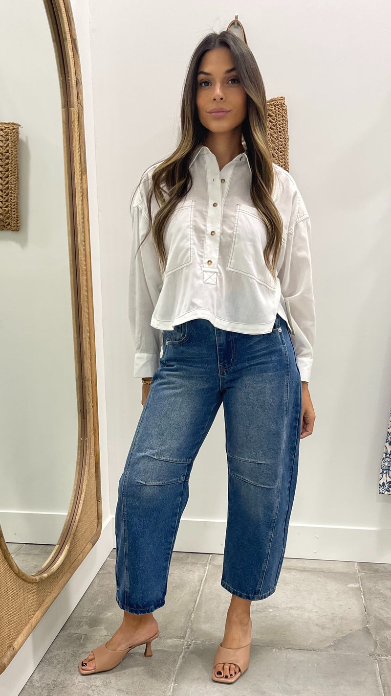 Woman wearing a white blouse and blue jeans standing in front of a mirror.