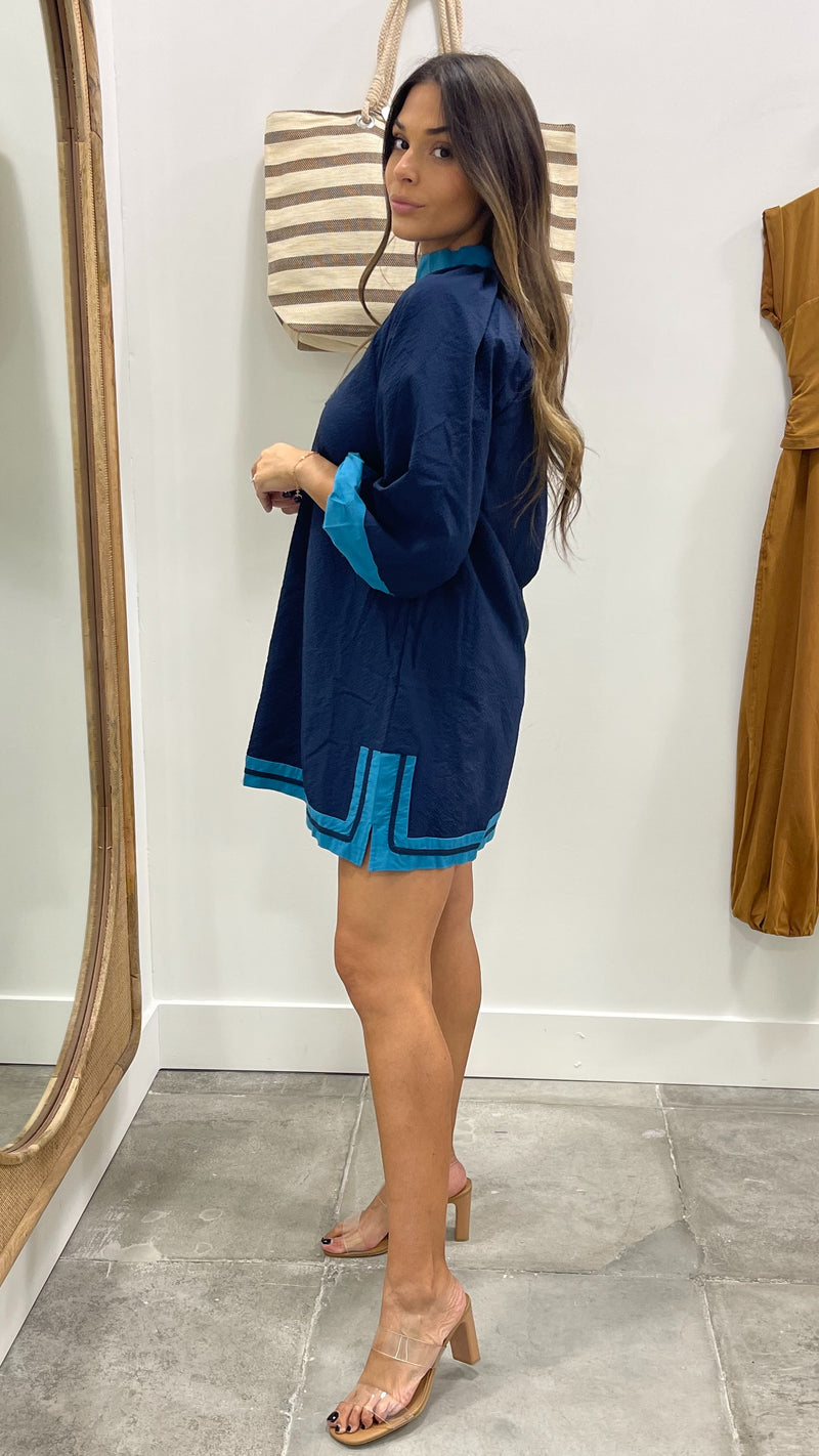 Woman wearing a blue outfit with turquoise trim in a fitting room.