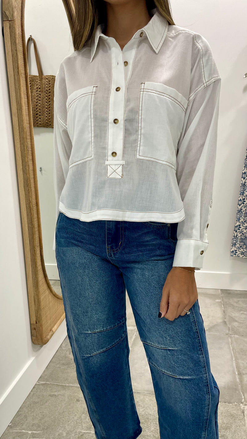 Person wearing a light-colored button-up shirt and blue jeans indoors.