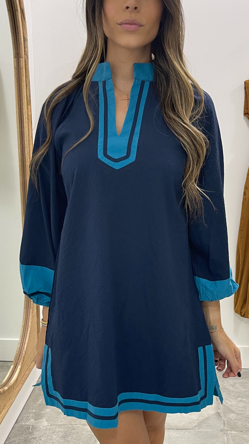 Woman wearing a navy dress with blue accents in front of a mirror.