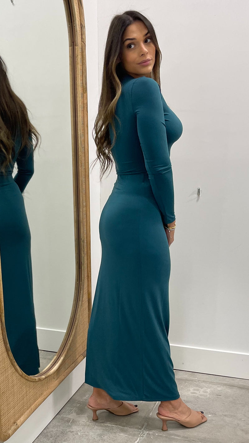 Woman in a teal dress standing in front of a mirror.