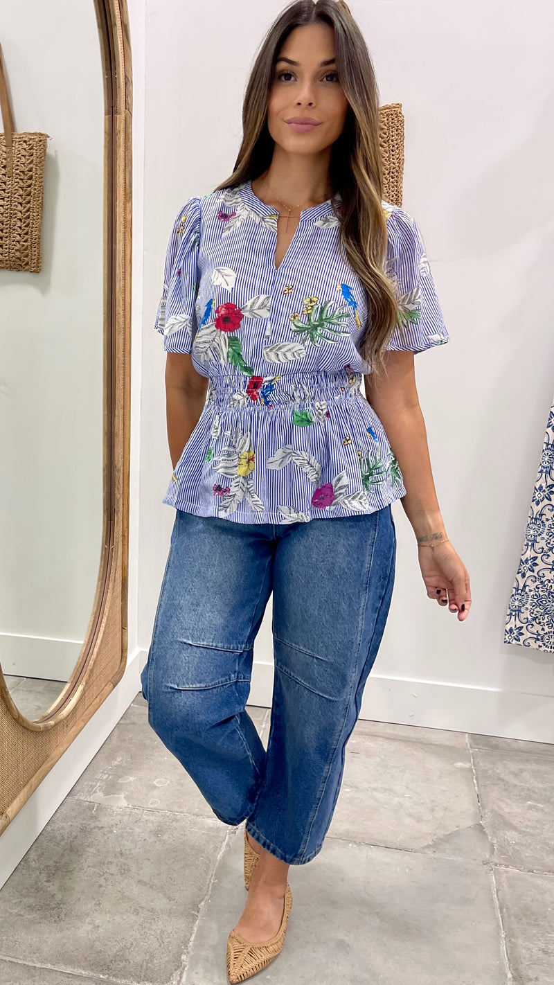 Woman wearing a floral blouse and blue jeans standing in front of a mirror.