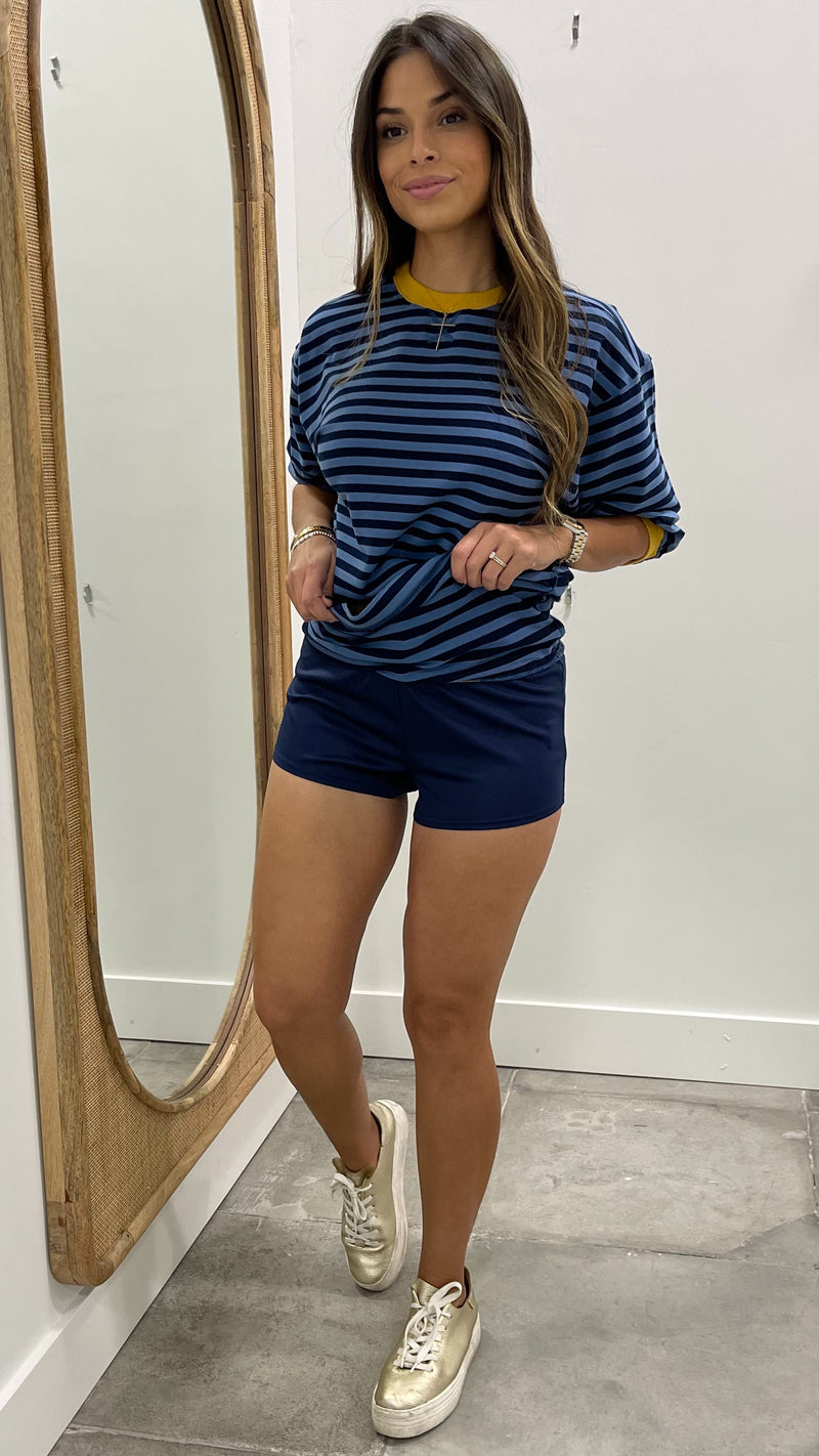 Woman wearing a blue and black striped shirt and shorts, standing in front of a mirror.