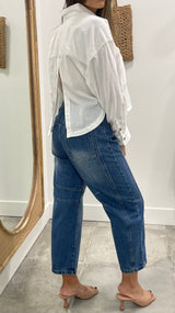 Person wearing a white blouse and blue jeans standing in front of a mirror.