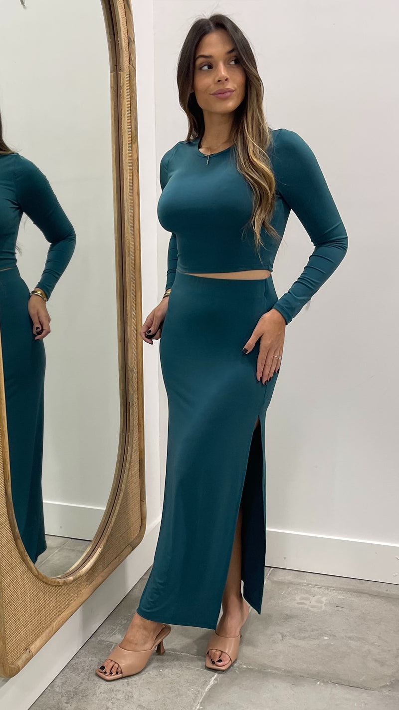 Woman in teal long-sleeve top and high-waisted skirt standing in front of a mirror.