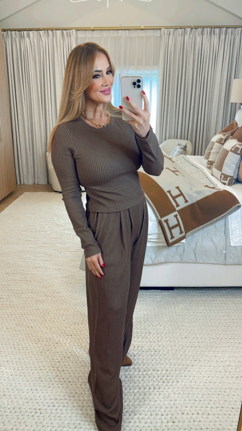 Woman taking a mirror selfie in a brown outfit in a bedroom.