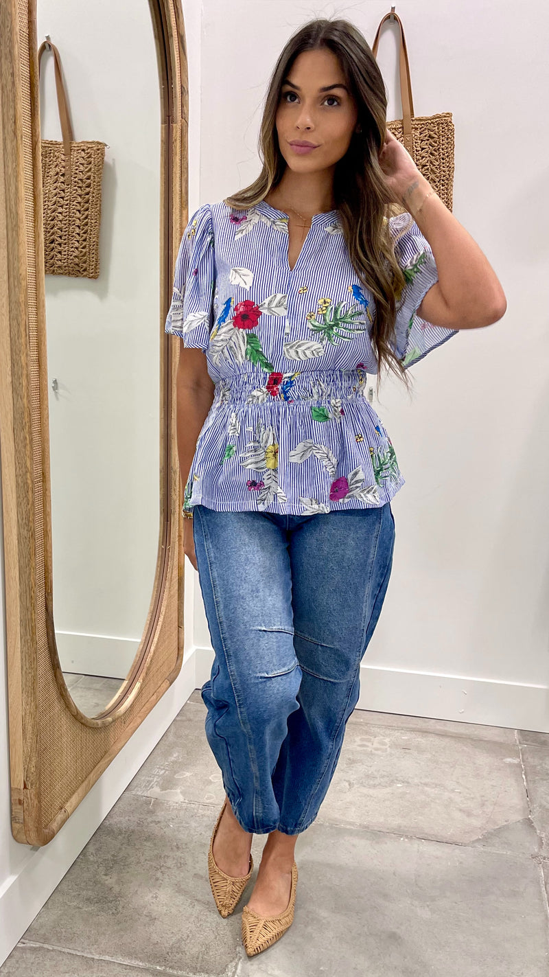 Woman wearing a floral blouse and jeans standing in front of a mirror.