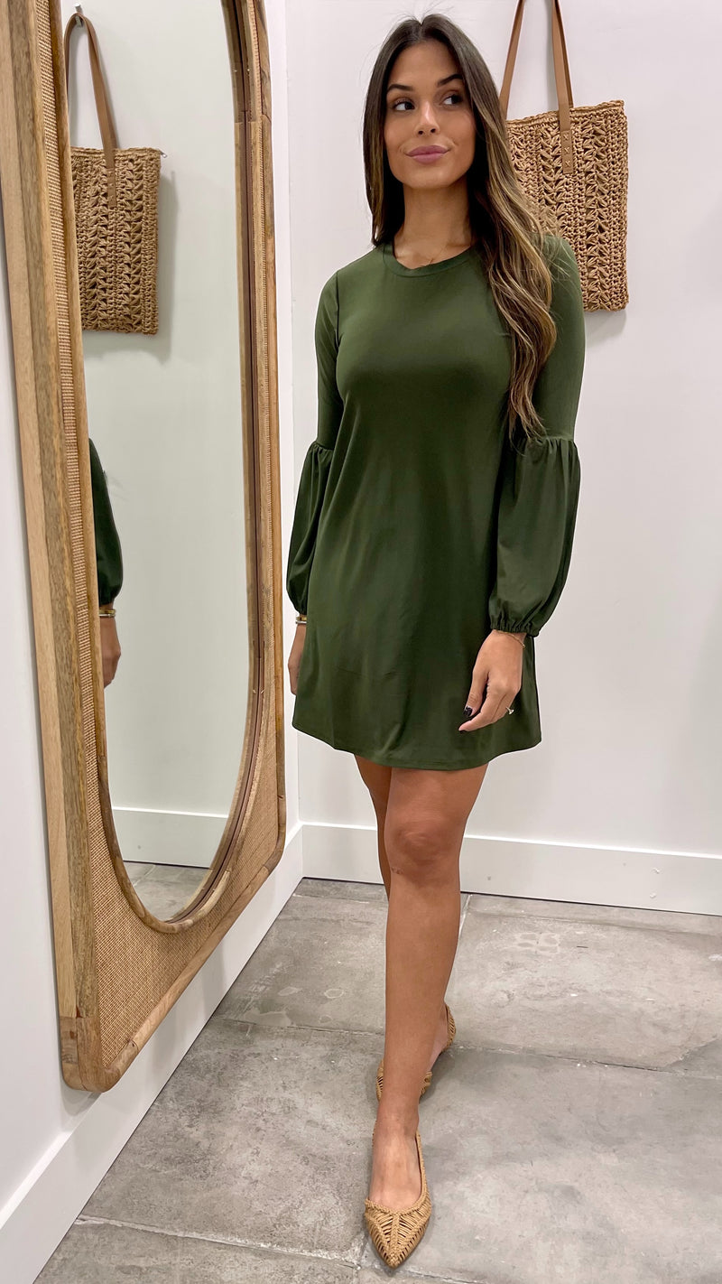 Woman wearing a green dress standing in front of a mirror.