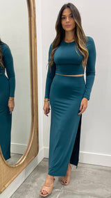 Woman wearing a teal long-sleeve top and skirt standing in front of a mirror.