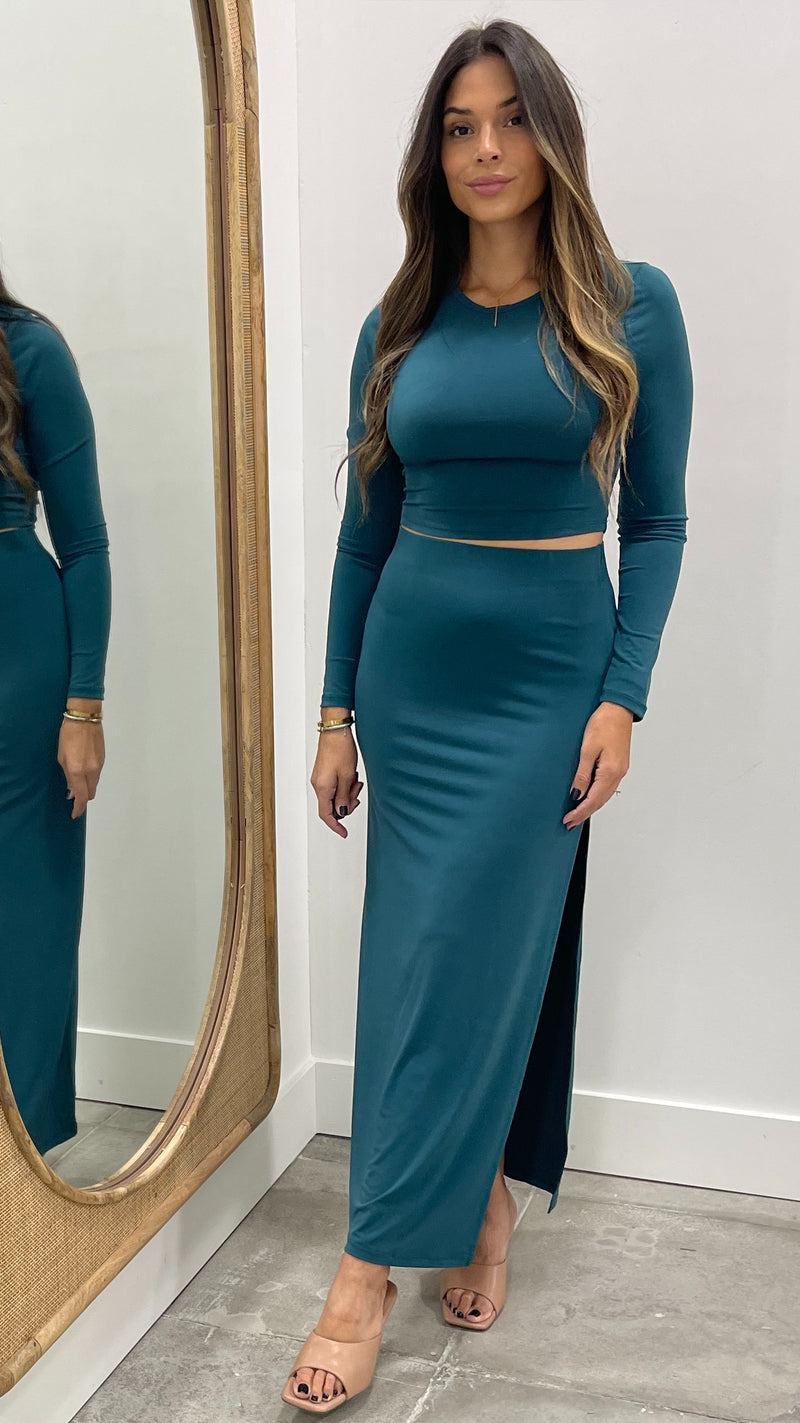 Woman wearing a teal long-sleeve top and skirt standing in front of a mirror.
