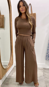 Woman wearing a brown ribbed top and wide-leg pants standing in front of a mirror.