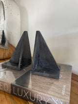 Black triangular shelf bracket on a wooden surface with a magazine in the background.