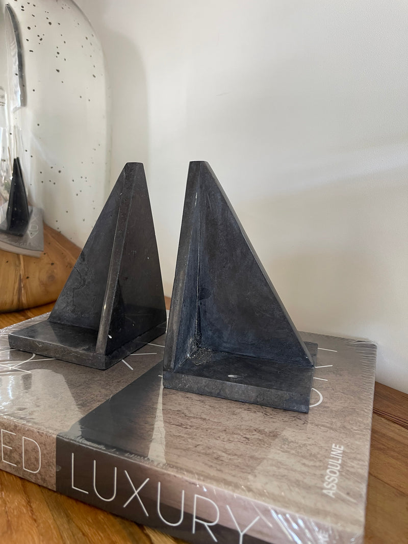 Black triangular shelf bracket on a wooden surface with a magazine in the background.