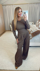 Woman taking a mirror selfie wearing a brown outfit in a room with a neutral color scheme.