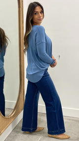 Woman wearing a blue top and dark blue jeans standing in front of a mirror.